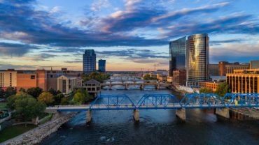 Downtown Grand Rapids aerial with Grand River and bridges during sunset, with a beautiful cloudscape in the background, and the Blue Bridge pedestrian bridge in the foreground.